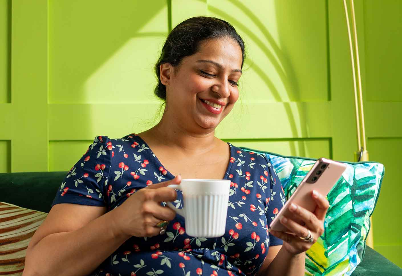 Woman smiling while holding a cup and looking at her phone